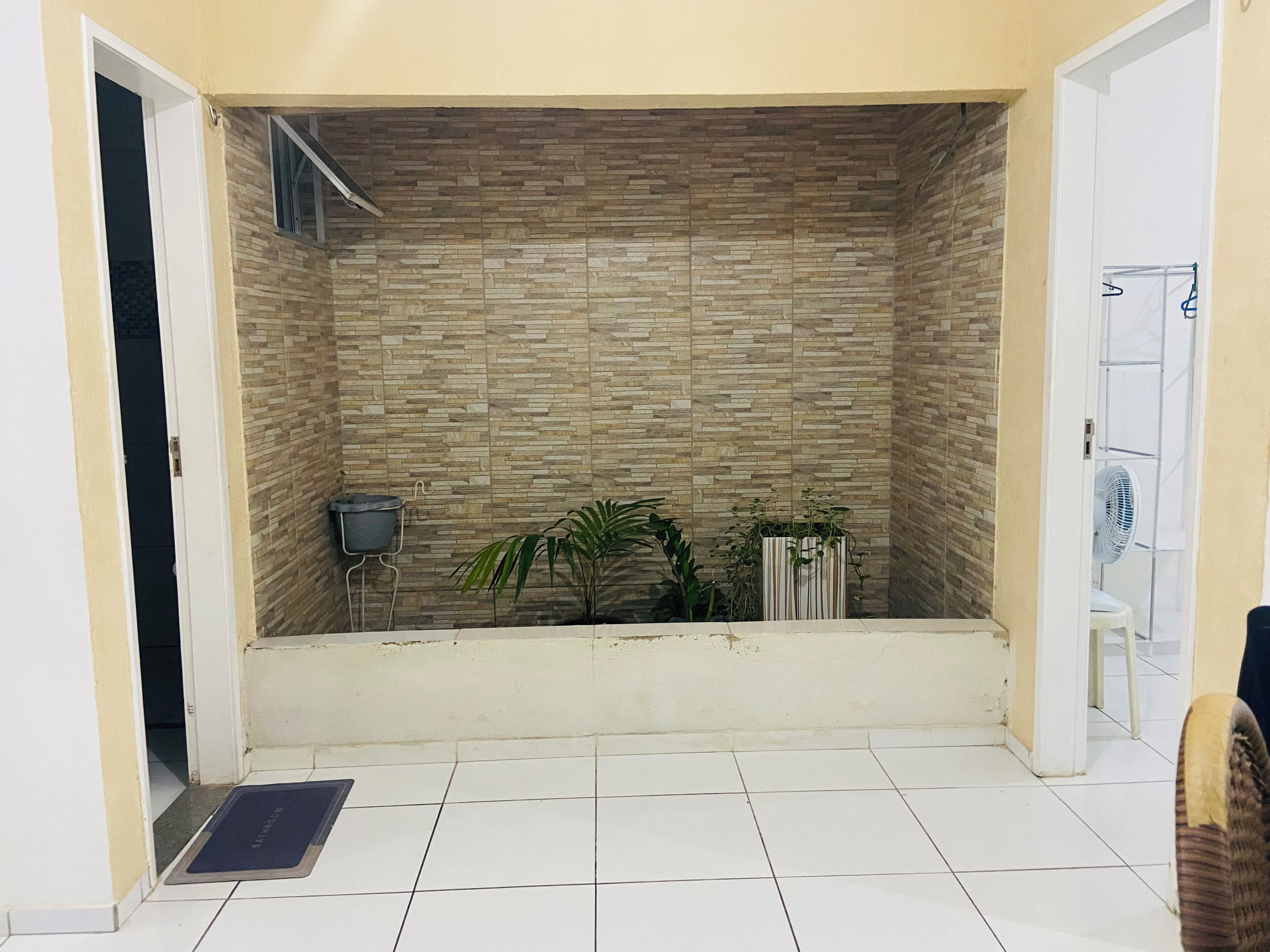 A room with a tiled floor, a stone-patterned wall, a small trash bin, and a potted plant.