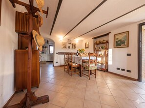 A dining area with a table set for four, wooden chairs, a bookshelf, and a kitchen in the background. - Villa with a garden in the heart of Monferrato (Piemonte)