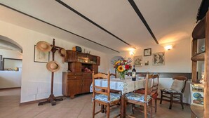 Comedor con una mesa dispuesta para cuatro, sillas de madera, un armario con adornos y un reloj de pared.
