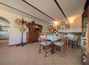 A dining area with a table set for four, wooden chairs, a cabinet with decorative items, and a wall clock. - Villa with a garden in the heart of Monferrato (Piemonte)