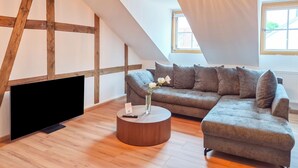 Une pièce de style loft avec des poutres en bois apparentes, un canapé d’angle, une table basse ronde et une grande fenêtre.