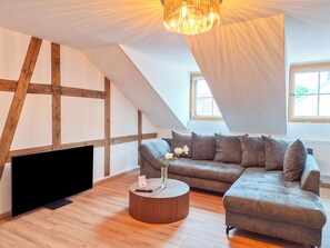Ein Loft-Zimmer mit freiliegenden Holzbalken, einem Ecksofa, einem runden Couchtisch und einem großen Fenster.