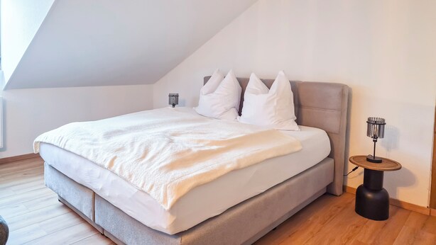 Une chambre à coucher avec un grand lit, une table de chevet, une lampe et un plafond en pente.
