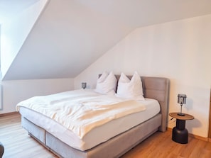 A bedroom with a large bed, a bedside table, a lamp, and a sloped ceiling. - Elisabeth Apartment in a half-timbered house from 1596 – Jena’s Old Town (Jena)