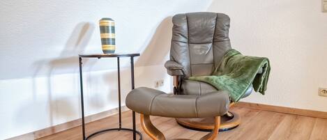 Una habitación moderna con un sillón de cuero, una mesita auxiliar pequeña y un taburete de madera original.