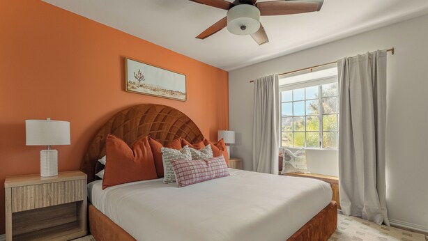 A bedroom with a large bed, wooden headboard, two bedside tables with lamps, a ceiling fan, and a window with curtains. - Desert Dreams: private pool, sauna, cold plunge, star dome, gym and theatre (Yucca Valley)