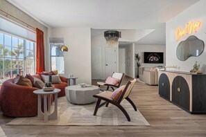 A modern living room with a large window, a red sofa, a round coffee table, and a unique chandelier. - Desert Dreams: private pool, sauna, cold plunge, star dome, gym and theatre (Yucca Valley)