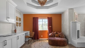 A modern living room with a fireplace, a round ottoman, and a large window with curtains. - Desert Dreams: private pool, sauna, cold plunge, star dome, gym and theatre (Yucca Valley)
