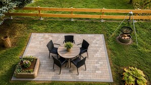 A patio with a round table and chairs, surrounded by a brick border, with a wooden fence in the background. - Modern Vacation Rental in Idar-Oberstein (Algenrodt) (Idar-Oberstein)