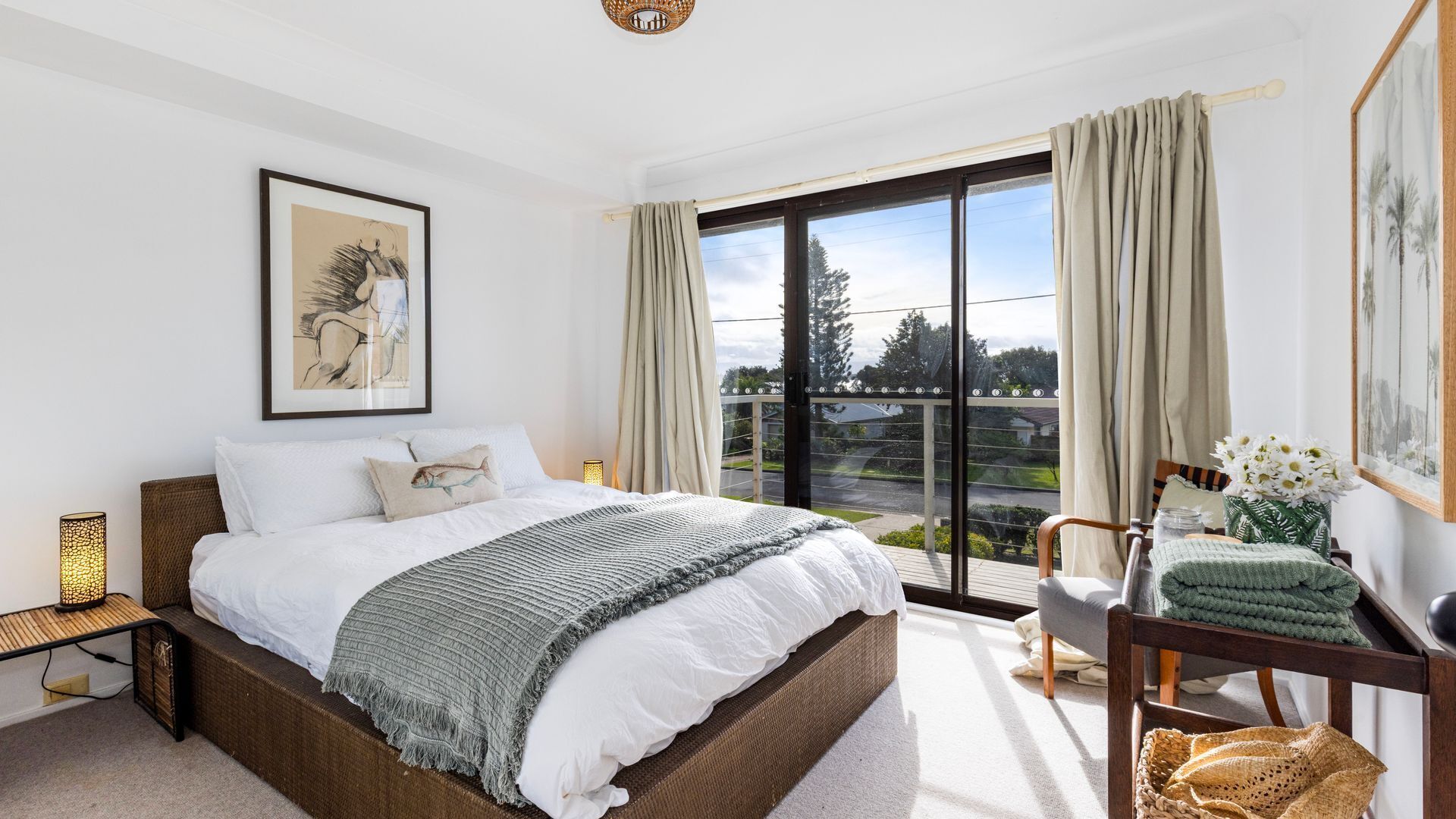 A bedroom with a large bed, a window with curtains, a chair, and a small table with a lamp.