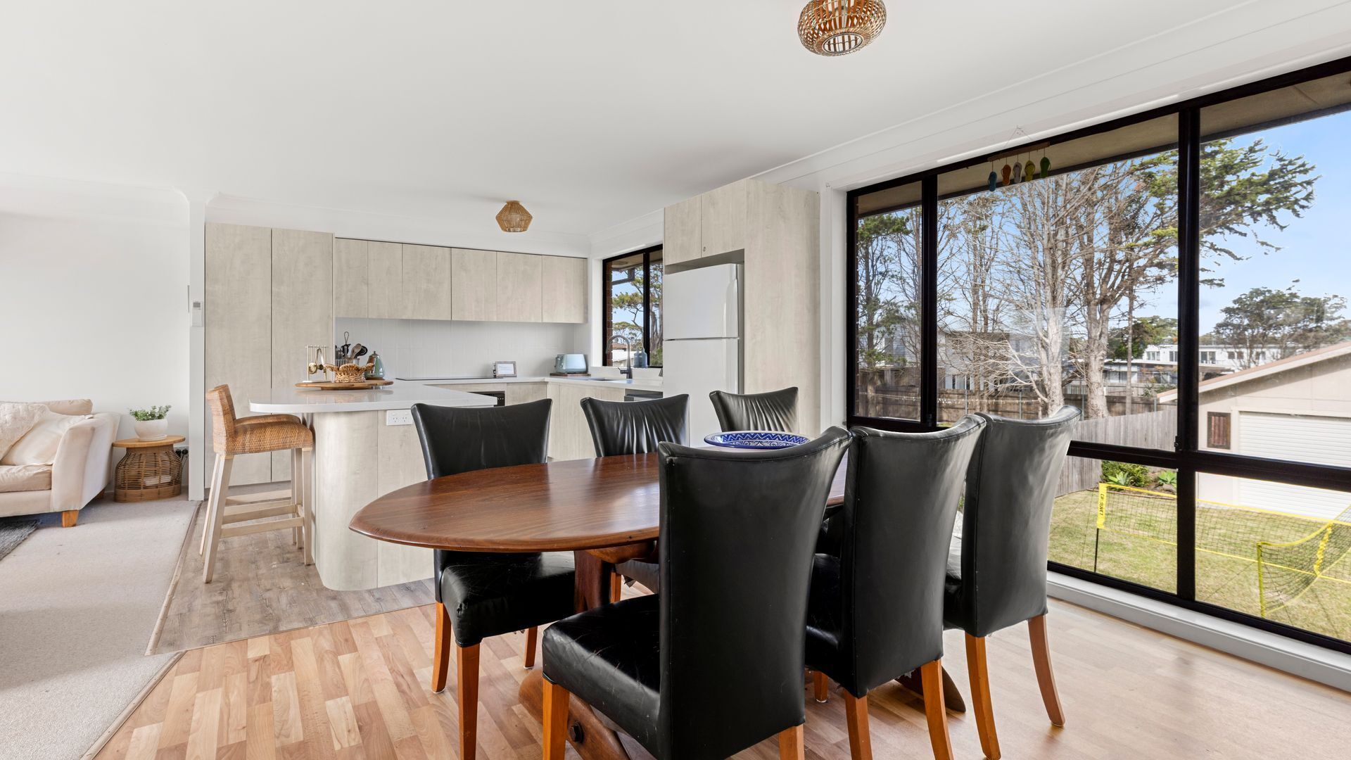 A modern kitchen with a dining area, large windows, and a view of the outdoors.