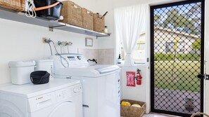 A laundry area with a Bosch washing machine, a dryer, and a shelf with baskets. - The Beach Bach - Pet Friendly with Firepit (Culburra Beach)