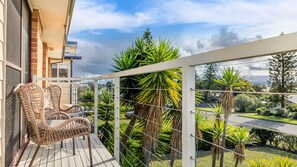 A balcony with wicker furniture, a view of a residential area, and a clear sky. - The Beach Bach - Pet Friendly with Firepit (Culburra Beach)