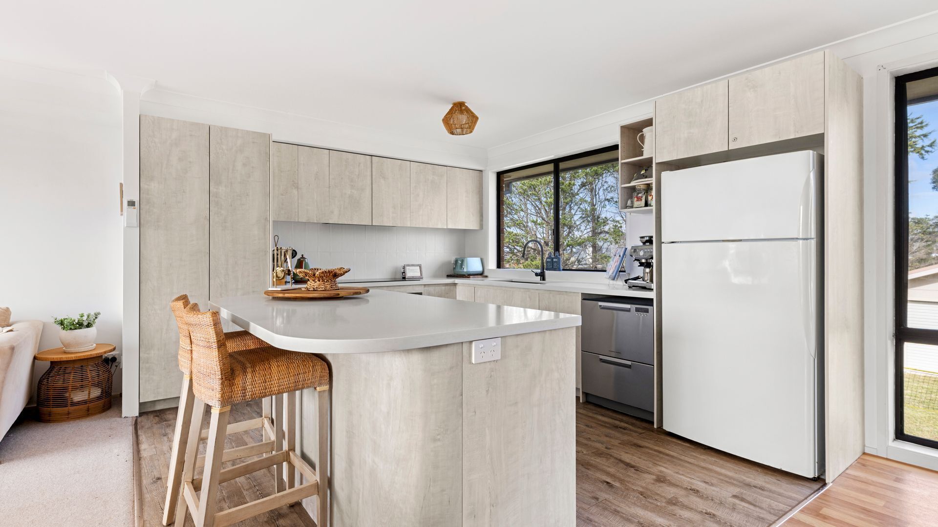 A modern kitchen with a large island, stainless steel appliances, and a view through the window.
