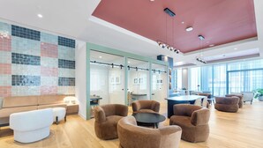 Ein moderner Lounge-Bereich mit Holzboden, Glastrennwand und vielfältigen Sitzgelegenheiten, darunter Sofas und Sessel.