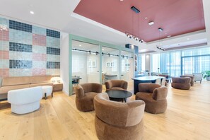 Ein moderner Lounge-Bereich mit Holzboden, Glastrennwand und vielfältigen Sitzgelegenheiten, darunter Sofas und Sessel.