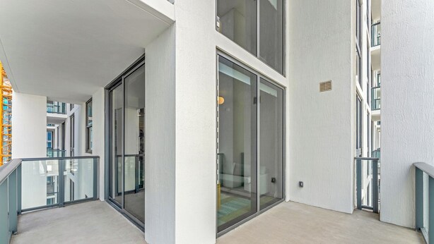 Ein modernes Gebäude mit Glastür, einem Balkon mit Metallgeländer und einem Betonboden.