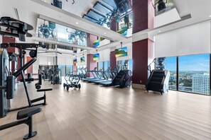 Ein großzügiger Fitnessraum mit unterschiedlichen Trainingsgeräten, großen Fenstern und Blick auf die Stadt.
