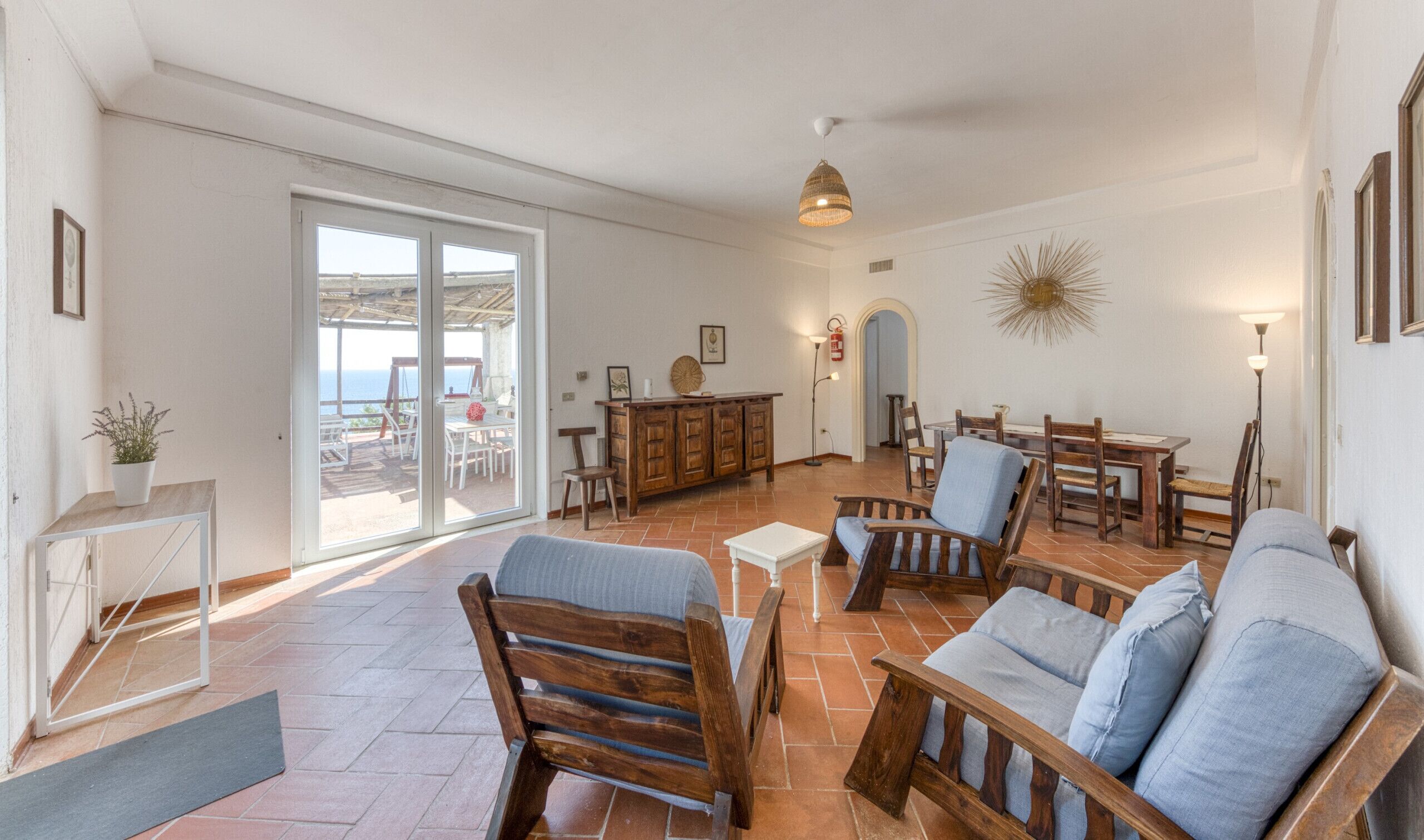 Un vaste espace de vie avec une grande porte-fenêtre coulissante donnant sur un patio extérieur, des meubles en bois et un luminaire suspendu au plafond.