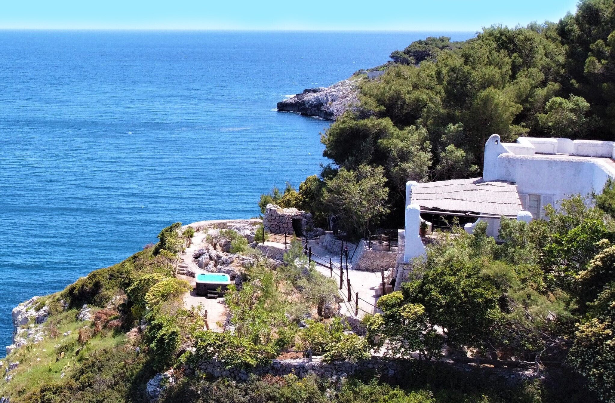 A coastal property with a stone pathway leading to a white building with a blue roof, overlooking the sea.