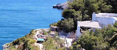 A coastal property with a stone pathway leading to a white building with a blue roof, overlooking the sea.