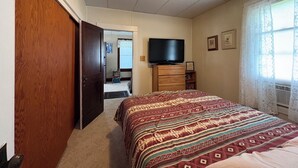 Quarto com cama, penteadeira, televisão e porta que dá para outro espaço.