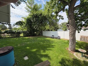 Ein Garten mit Rasen, einer Holzterrasse, einem Baum und einem weißen Zaun.