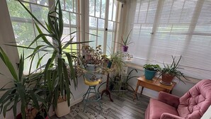 Uma sala de estar aconchegante com uma mesa de centro de vidro, uma poltrona rosa e várias plantas em vasos.