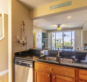 A kitchen with a dishwasher, wooden cabinets, a black countertop, and a view of the outside. - 2 mins from beach, waterfront views, sleeps 7 (Ruskin)