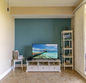 A living room with a TV on a white stand, a small table with a Wi-Fi sign, and a white shelving unit. - 2 mins from beach, waterfront views, sleeps 7 (Ruskin)