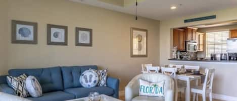 Un salon avec un canapé, une table basse et un fauteuil agrémenté d’un coussin sur lequel est écrit « FLORIDE ».
