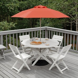 Een ronde buitentafel met witte stoelen en een rode parasol op een houten terras.