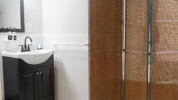 A bathroom with a white sink, dark cabinets, a wooden floor, and a shower area with a woven partition.