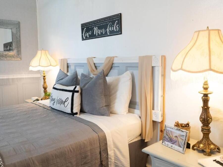A neatly made bed with a headboard, two bedside lamps, a framed picture, and a decorative lamp on a bedside table.