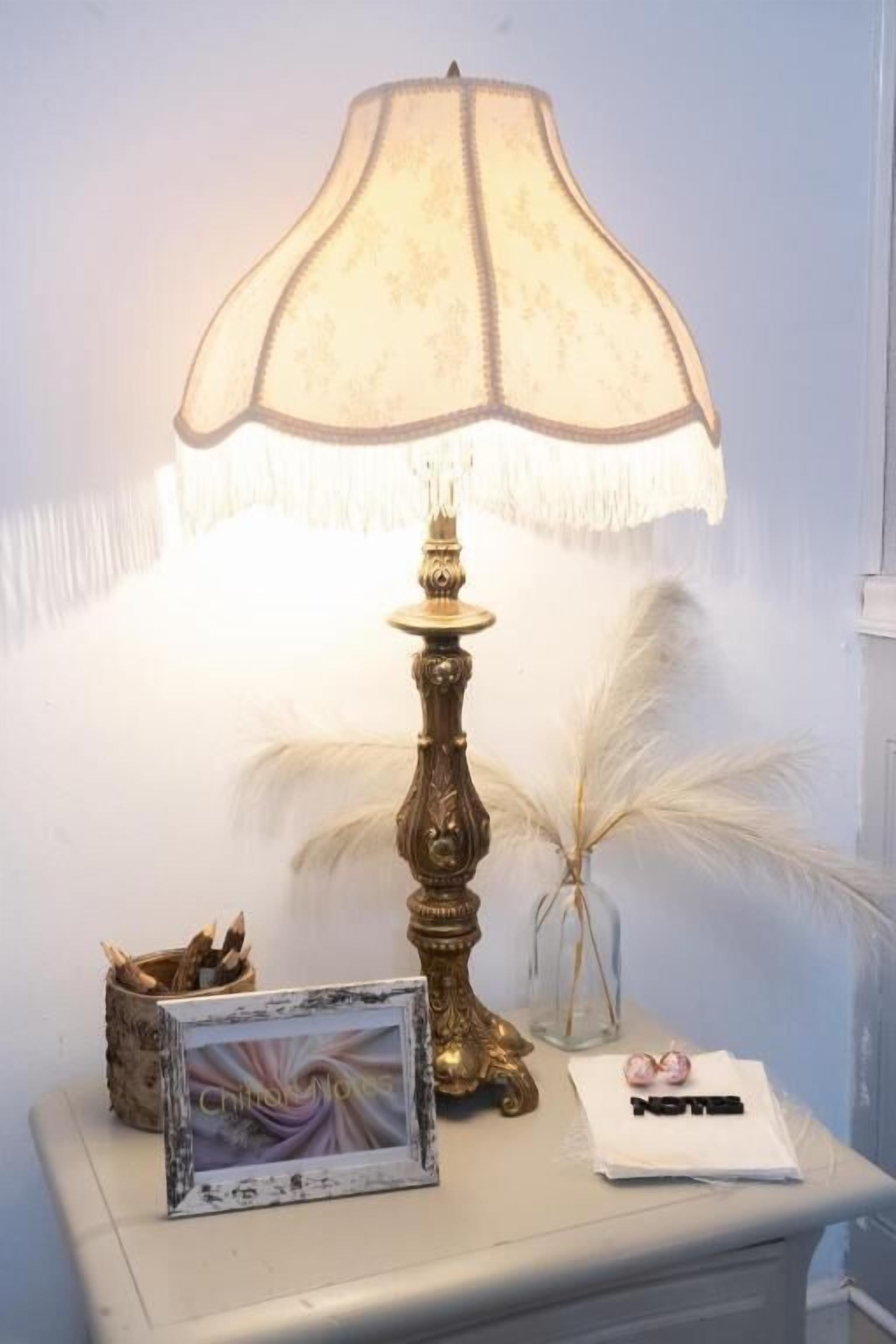 Een tafel met een lamp, een lijst met een afbeelding en een vaas met veertjes.