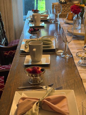 Una mesa de comedor con platos, cubiertos y un cuenco de fruta.