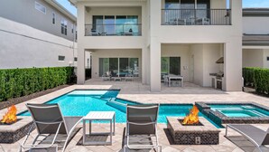 Un edificio moderno de dos pisos con un área de piscina que incluye sillones de descanso y una chimenea.