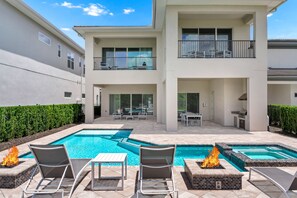 A modern two-story building with a swimming pool area featuring lounge chairs and a fire feature. - Elegant Home near Disney with Resort & Waterpark Access - 1002JN (Kissimmee)