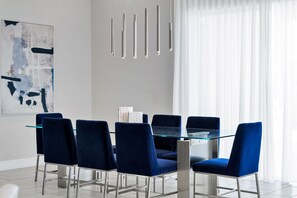 A modern dining area with a glass table and dark blue upholstered chairs. - Elegant Home near Disney with Resort & Waterpark Access - 1002JN (Kissimmee)