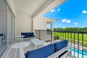 Ein Balkon mit Pool, weißen Möbeln und Blick auf einen Golfplatz.