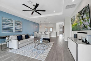 A modern living room with a white sofa, a coffee table, and a TV on a stand. - Elegant Home near Disney with Resort & Waterpark Access - 1002JN (Kissimmee)