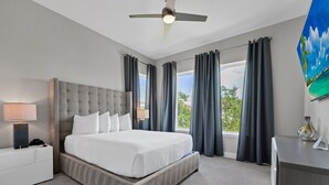 Una habitación de hotel con una cama grande, un escritorio, un ventilador de techo y una ventana con cortinas.