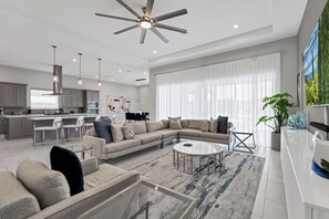A modern living room with a sectional sofa, a coffee table, and a dining area with chairs. - Elegant Home near Disney with Resort & Waterpark Access - 1002JN (Kissimmee)