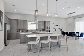 A modern kitchen with grey cabinets, a central island, bar stools, and pendant lighting. - Elegant Home near Disney with Resort & Waterpark Access - 1002JN (Kissimmee)