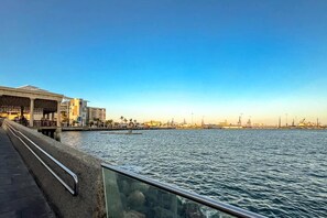 A waterfront promenade with a modern building, a clear sky, and a calm sea. - GuestReady - Rosamar M Apartments (Las Palmas de Gran Canaria)