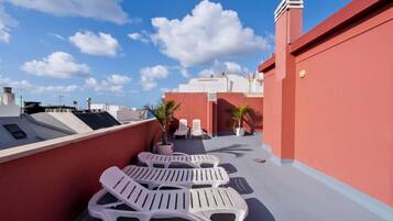 A rooftop terrace with white lounge chairs, potted plants, and a clear blue sky.