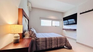 A bedroom with a bed, a bedside lamp, a TV mounted on the wall, and a window. - Cancun Bella & Vista Apartment Deluxe (Cancun)