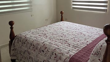 A bedroom with a bed, a ceiling fan, and two windows with blinds.