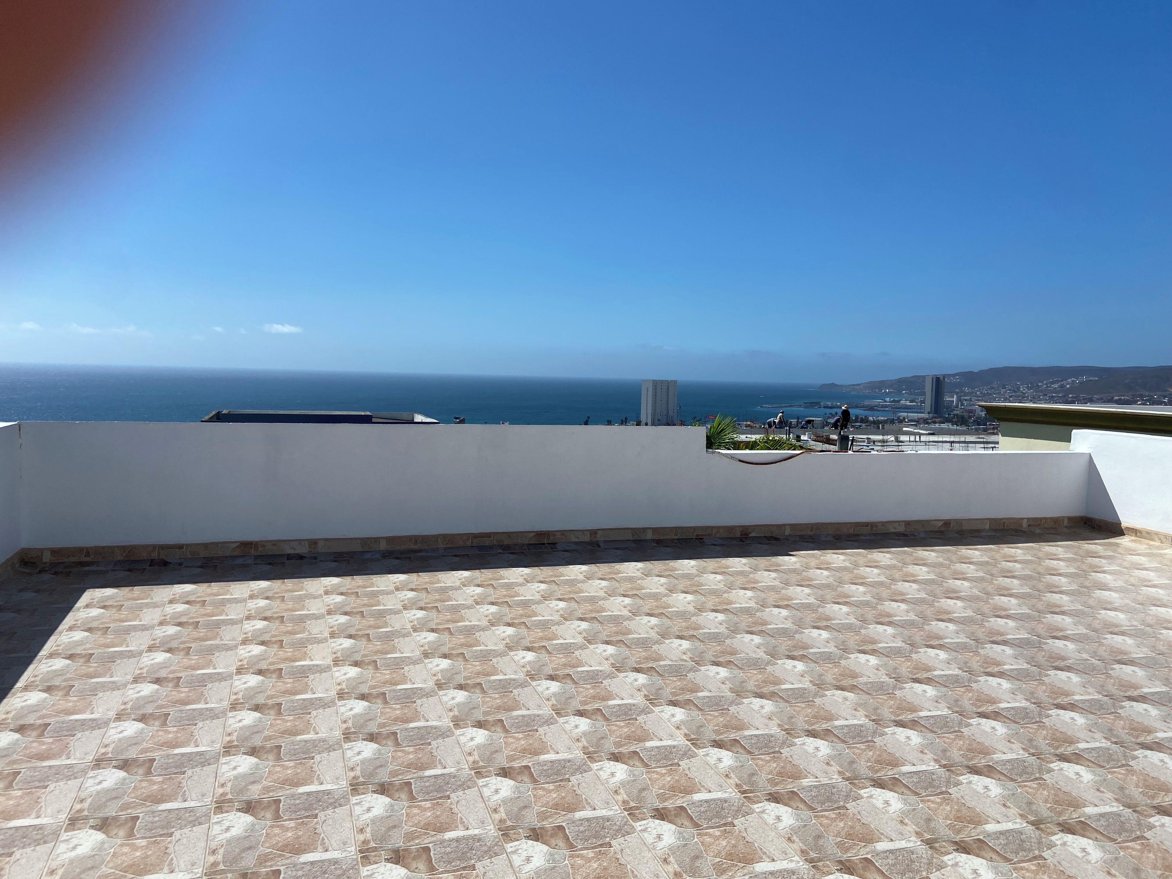 A rooftop terrace with a patterned floor, overlooking a coastal cityscape and the sea.