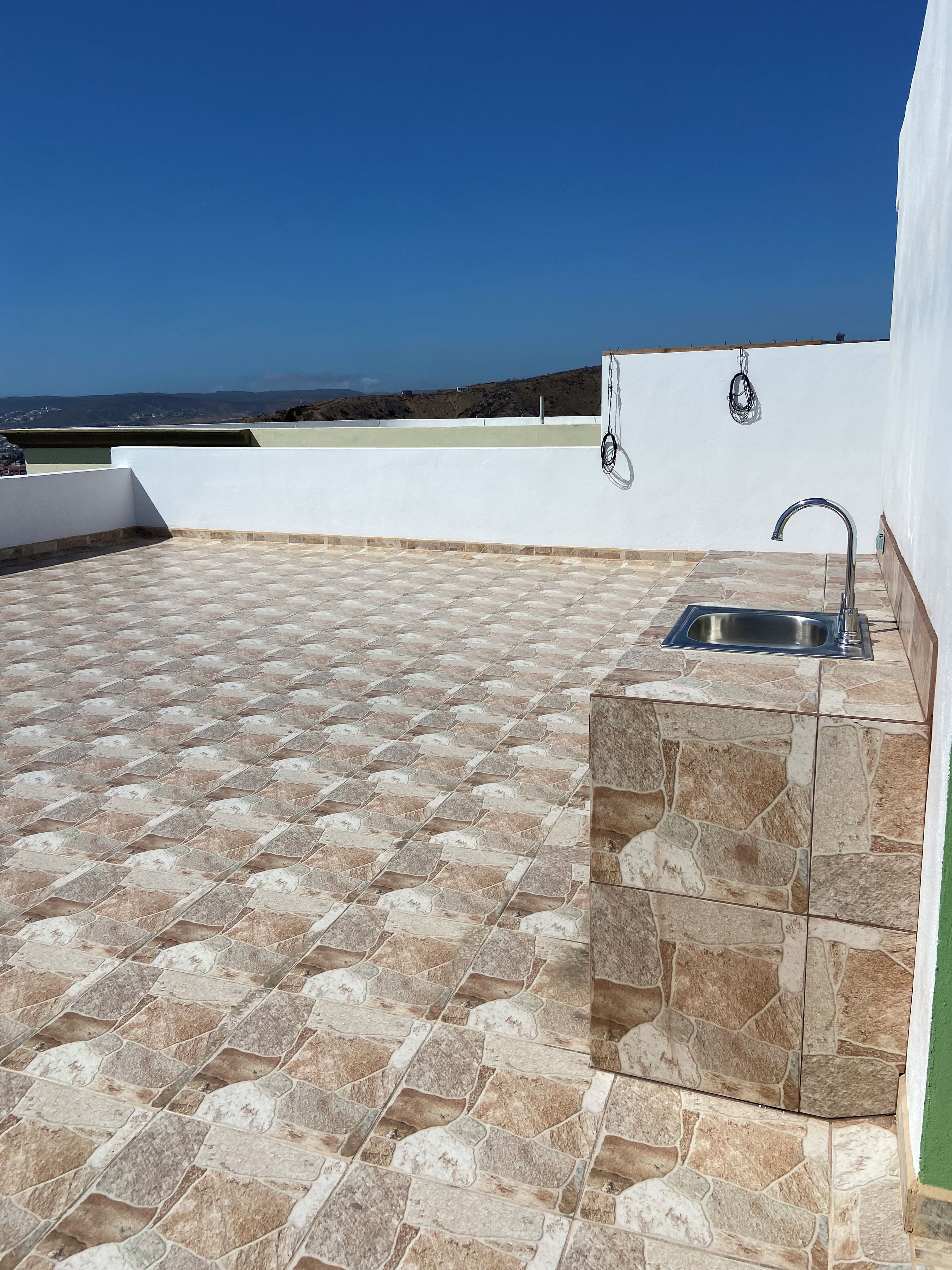 A rooftop patio with a stone-tiled floor, a built-in sink, and a view of the landscape.